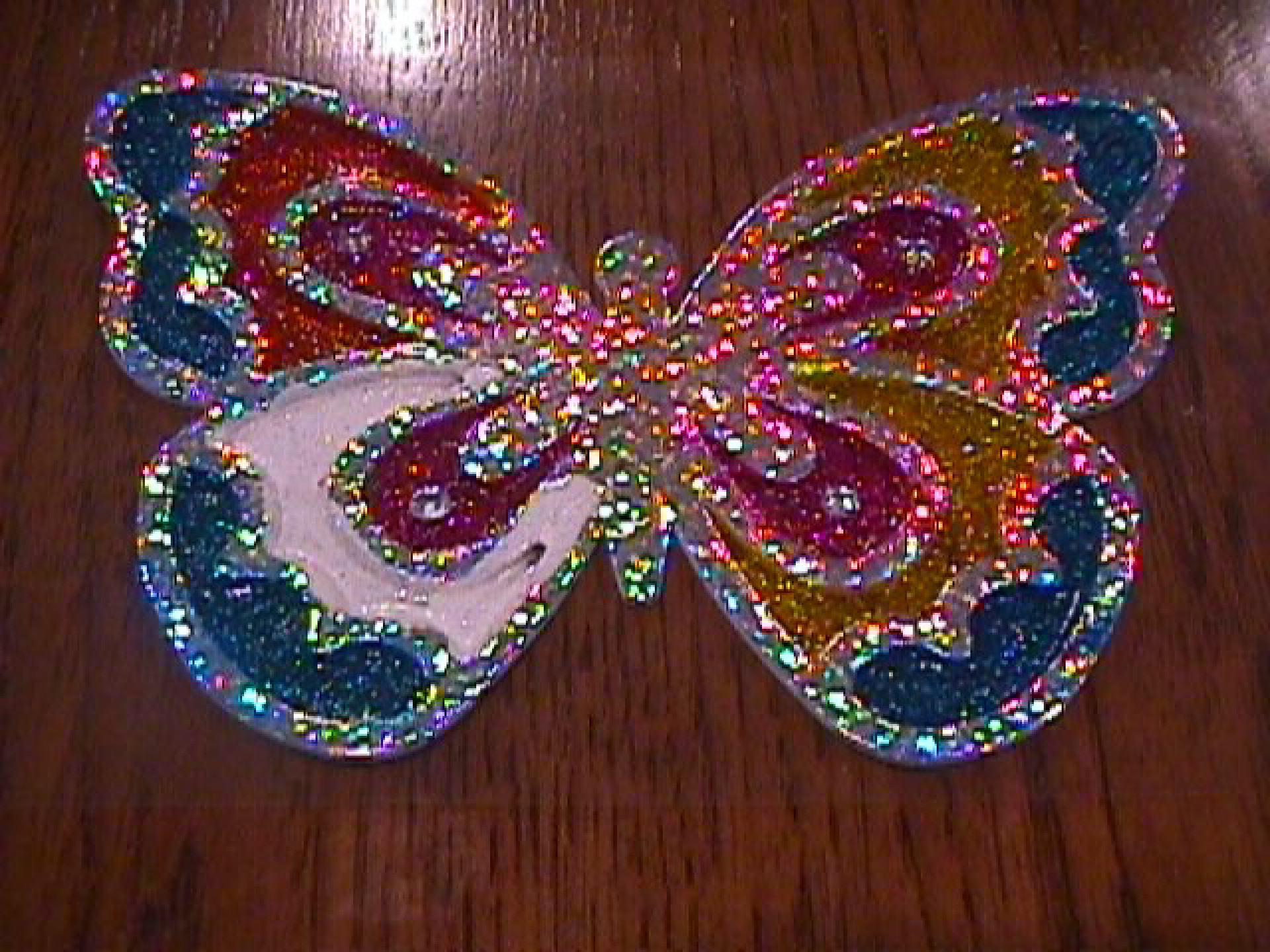 A rainbow butterfly, sparkle art project sitting on wood table