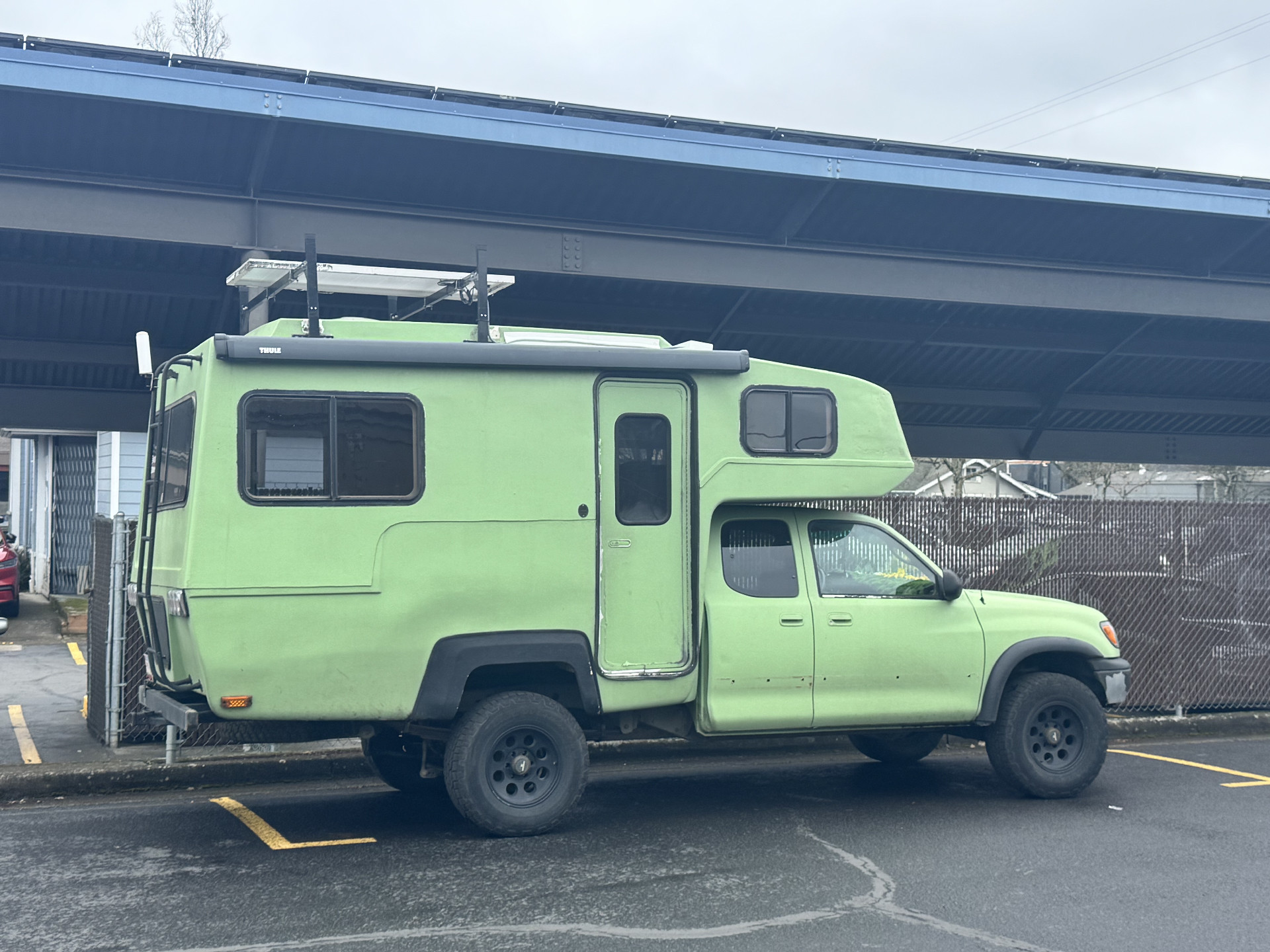 A camper truck with green camper on its back, solar panels, and a dash covered in plastic grass and glowers.